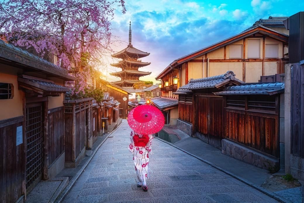 A woman in a kimono with a red umbrella on a lane leading to the Yasaka Pagoda in Kyoto, one of many things to do in Asia