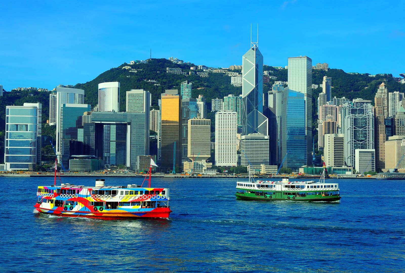 Ferries crossing Victoria Harbour in front of the Hong Kong Island skyline and green hills