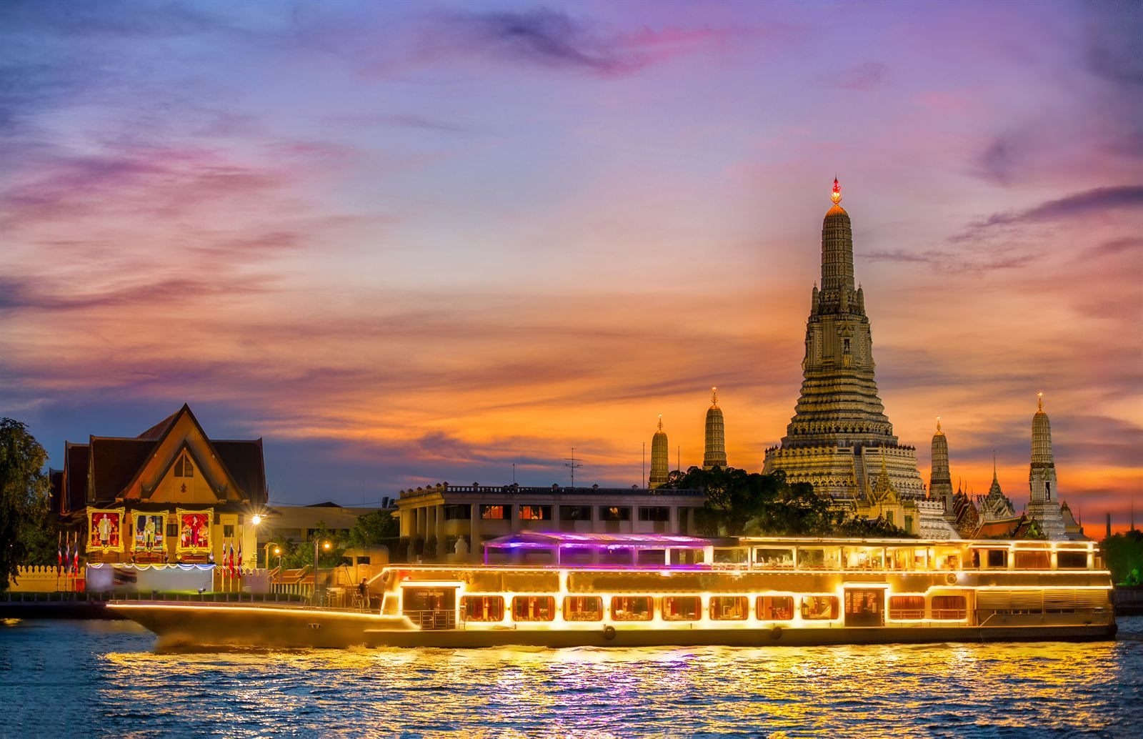 Wat Arun on the Chao Phraya River at sunset, with an illuminated boat passing, in Bangkok, one of the best places to visit in Asia